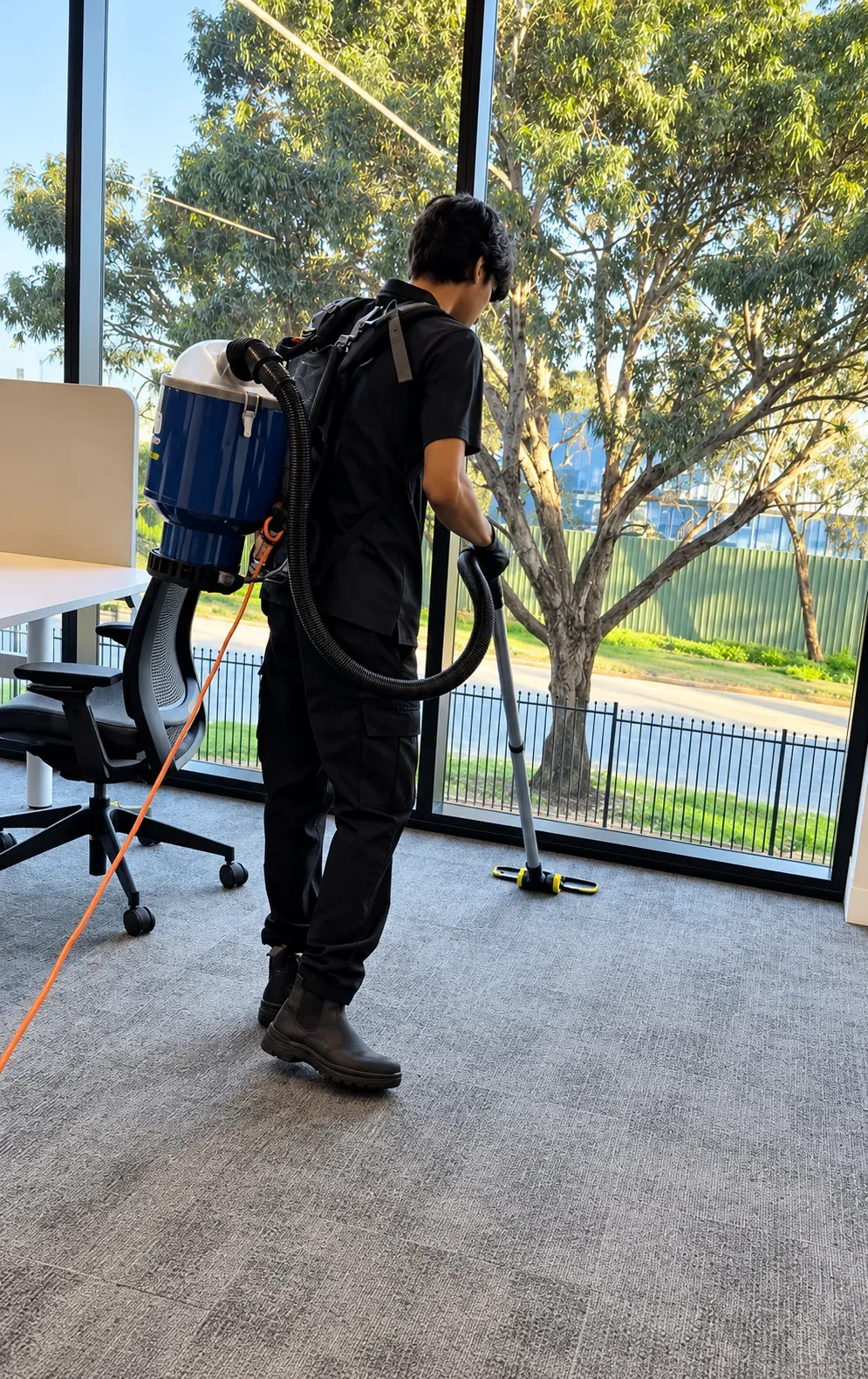HNT team member vacuuming office carpet with a backpack vacuum beside a window
